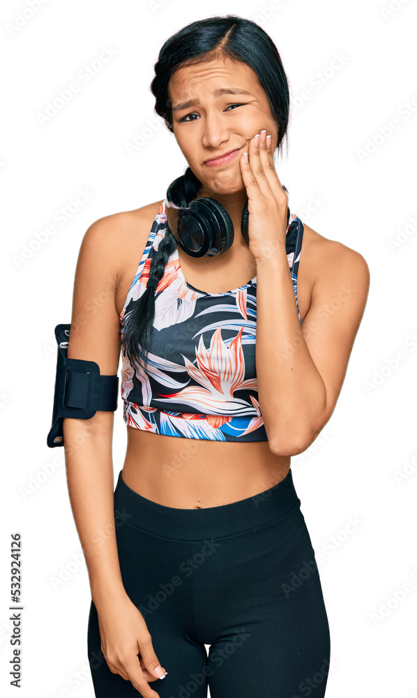 Beautiful hispanic woman wearing sportswear and headphones touching mouth with hand with painful expression because of toothache or dental illness on teeth. dentist Beautiful hispanic woman wearing sportswear and headphones touching mouth with hand with painful expression because of toothache or dental illness on teeth. dentist