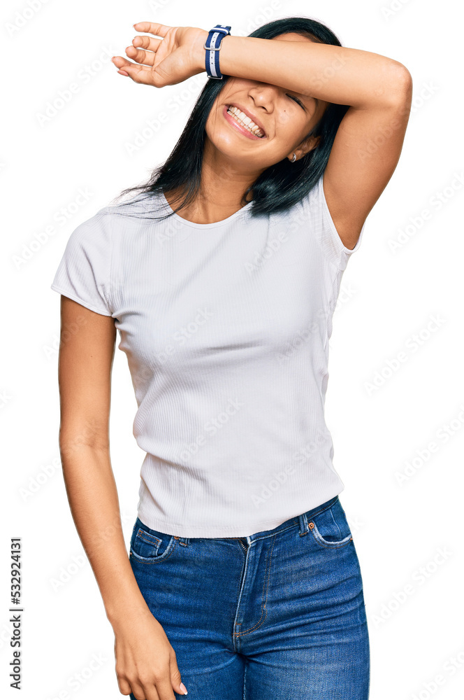 Beautiful hispanic woman wearing casual white tshirt covering eyes with arm smiling cheerful and funny. blind concept. Beautiful hispanic woman wearing casual white tshirt covering eyes with arm smiling cheerful and funny. blind concept.