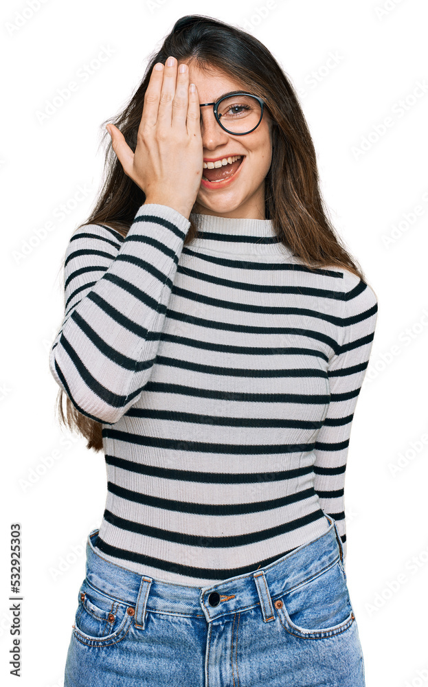 Young beautiful teen girl wearing casual clothes and glasses covering one eye with hand, confident smile on face and surprise emotion. Young beautiful teen girl wearing casual clothes and glasses covering one eye with hand, confident smile on face and surprise emotion.