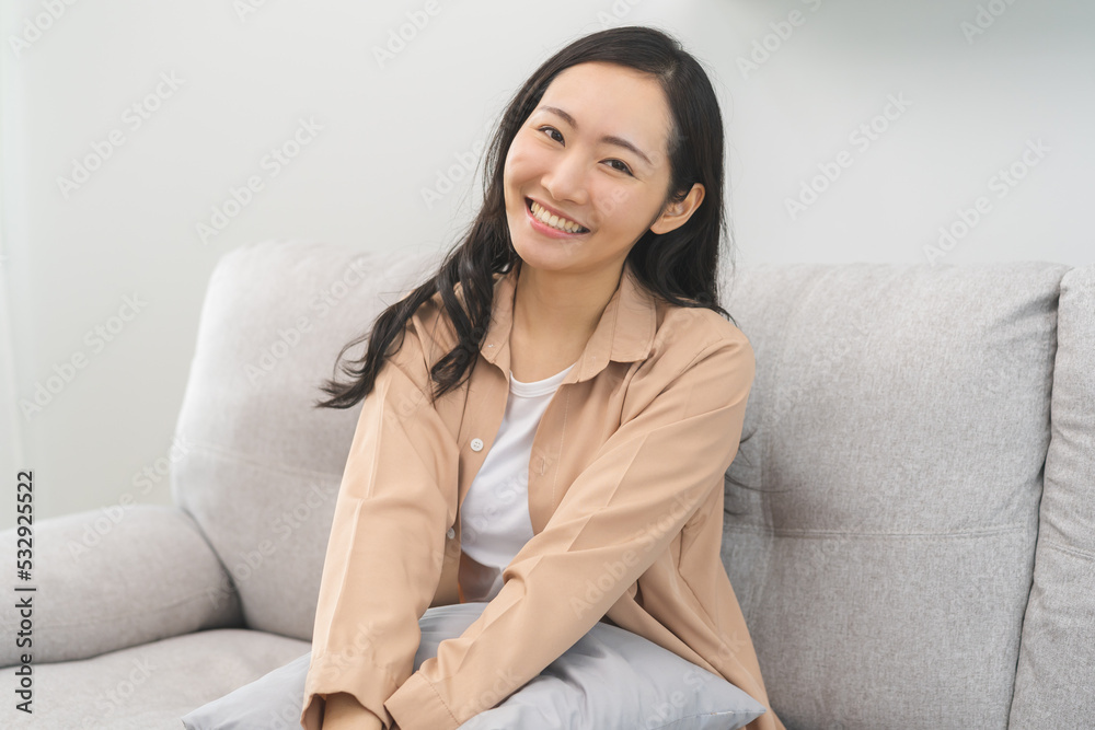 Smiling positive, attractive asian young woman in casual dress, pretty girl sitting on cozy sofa, couch rest, relax at home, portrait of beautiful with long black hair, feeling happy looking at camera Smiling positive, attractive asian young woman in casual dress, pretty girl sitting on cozy sofa, couch rest, relax at home, portrait of beautiful with long black hair, feeling happy looking at camera