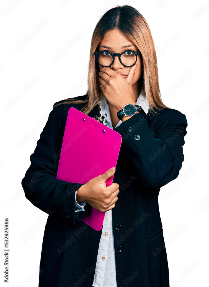 Young hispanic business woman holding clipboard with blank space shocked covering mouth with hands for mistake. secret concept. Young hispanic business woman holding clipboard with blank space shocked covering mouth with hands for mistake. secret concept.