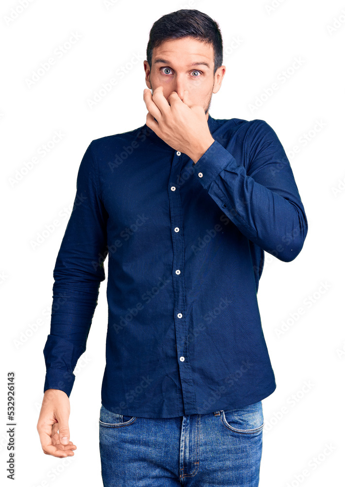 Young handsome man wearing casual shirt smelling something stinky and disgusting, intolerable smell, holding breath with fingers on nose. bad smell