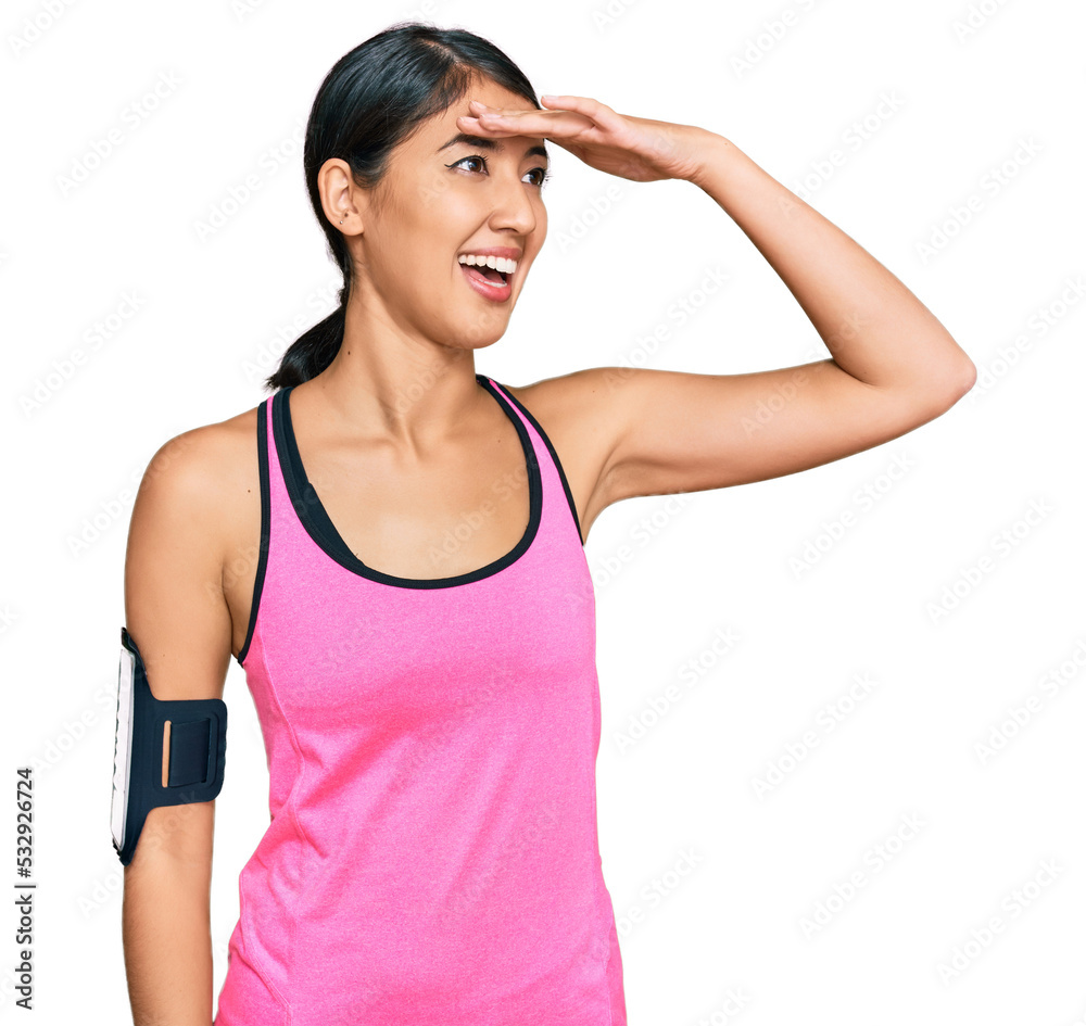 Beautiful asian young sport woman wearing sportswear and arm band very happy and smiling looking far away with hand over head. searching concept. Beautiful asian young sport woman wearing sportswear and arm band very happy and smiling looking far away with hand over head. searching concept.