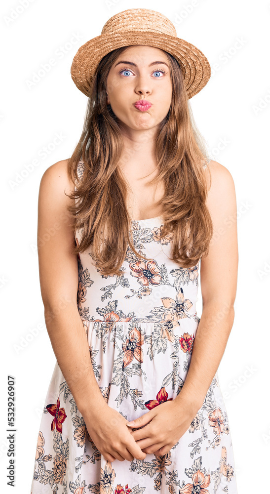 Beautiful caucasian young woman wearing summer hat puffing cheeks with funny face. mouth inflated with air, crazy expression. Beautiful caucasian young woman wearing summer hat puffing cheeks with funny face. mouth inflated with air, crazy expression.