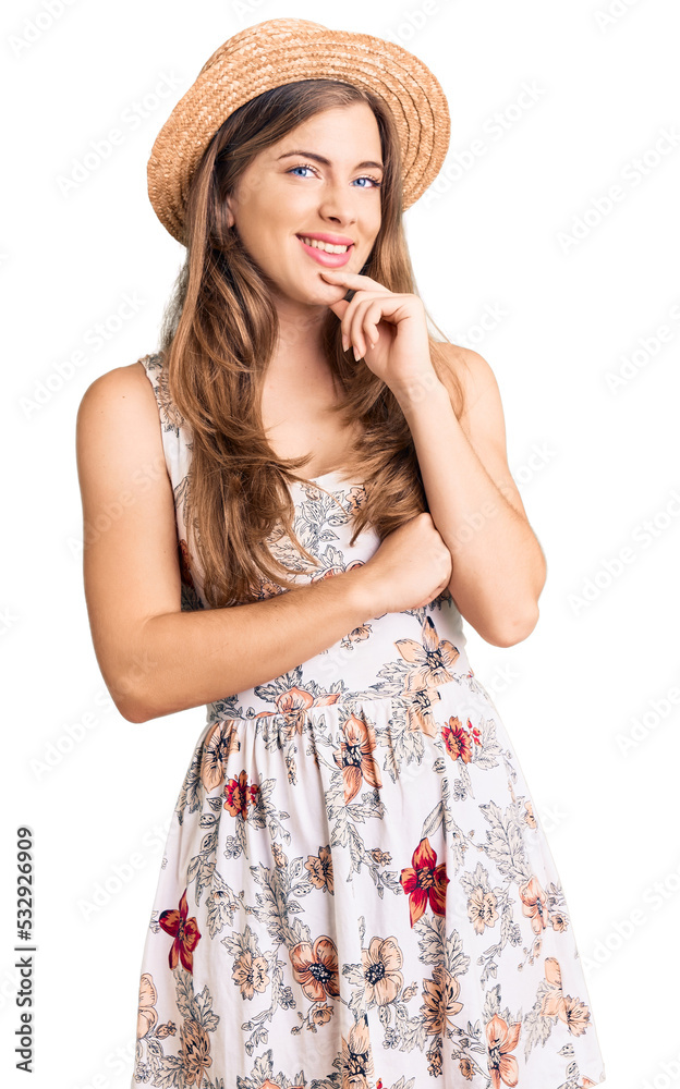 Beautiful caucasian young woman wearing summer hat looking confident at the camera with smile with crossed arms and hand raised on chin. thinking positive. Beautiful caucasian young woman wearing summer hat looking confident at the camera with smile with crossed arms and hand raised on chin. thinking positive.