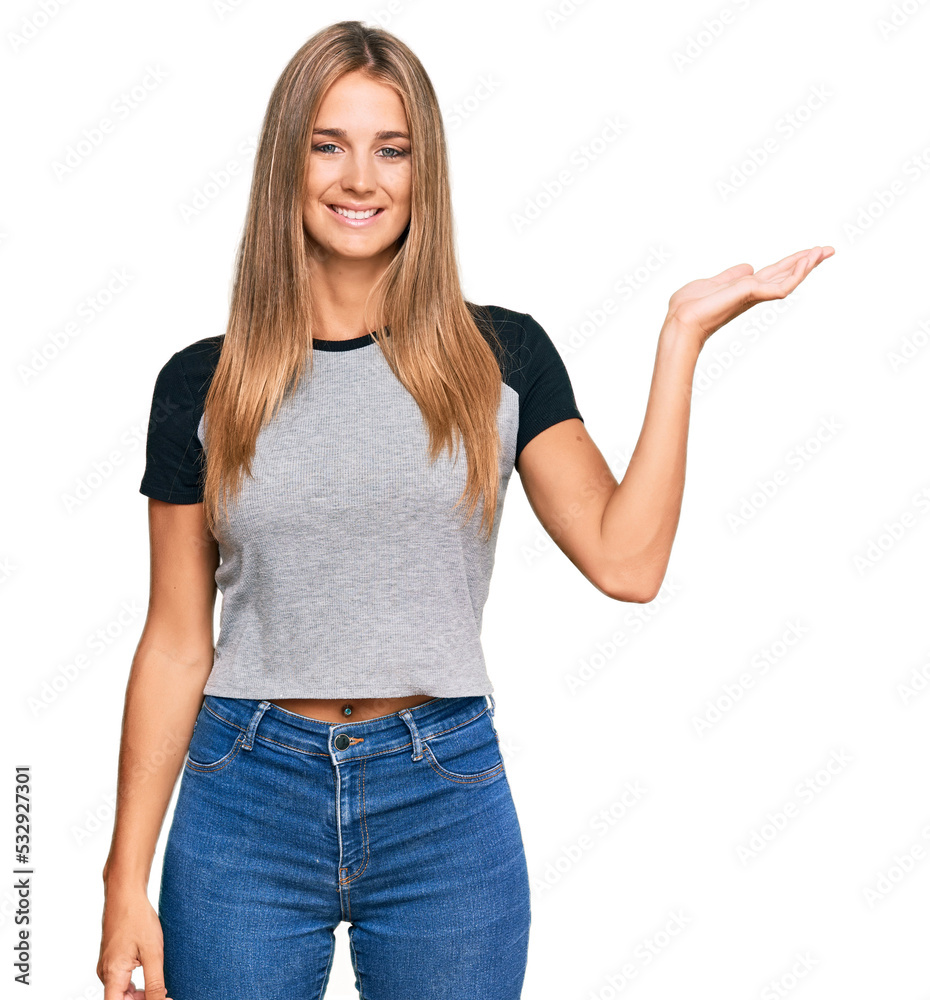 Young blonde woman wearing casual clothes smiling cheerful presenting and pointing with palm of hand looking at the camera. Young blonde woman wearing casual clothes smiling cheerful presenting and pointing with palm of hand looking at the camera.