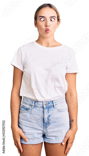 Young beautiful blonde woman wearing casual white tshirt making fish face with lips, crazy and comical gesture. funny expression.