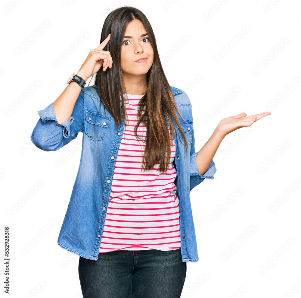 Young brunette woman wearing casual clothes confused and annoyed with open palm showing copy space and pointing finger to forehead. think about it. Young brunette woman wearing casual clothes confused and annoyed with open palm showing copy space and pointing finger to forehead. think about it.