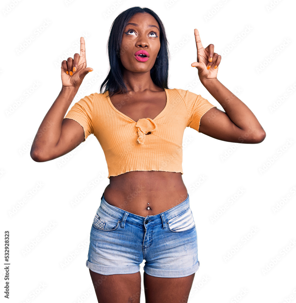Young african american woman wearing casual clothes amazed and surprised looking up and pointing with fingers and raised arms. Young african american woman wearing casual clothes amazed and surprised looking up and pointing with fingers and raised arms.