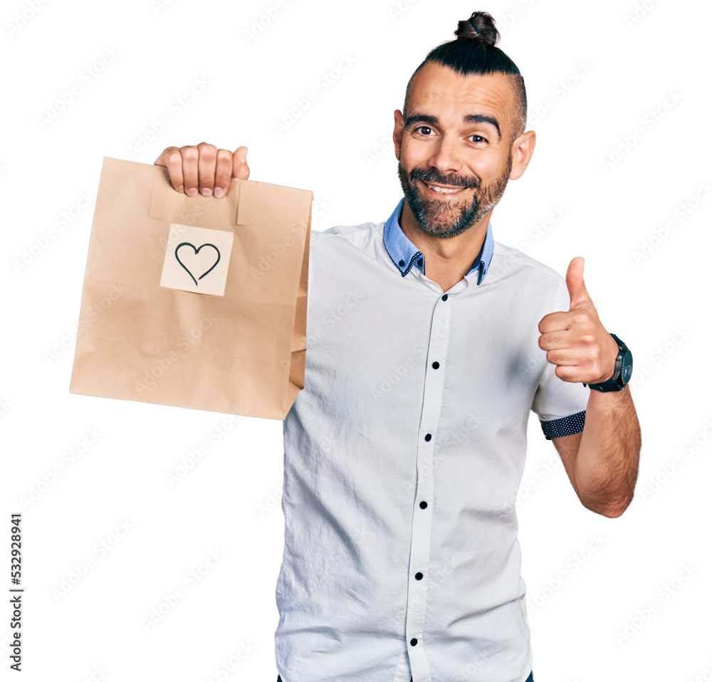 Hispanic man with ponytail holding take away paper bag with heart reminder smiling happy and positive, thumb up doing excellent and approval sign Hispanic man with ponytail holding take away paper bag with heart reminder smiling happy and positive, thumb up doing excellent and approval sign