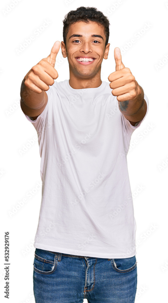 Fototapeta premium Young handsome african american man wearing casual white tshirt approving doing positive gesture with hand, thumbs up smiling and happy for success. winner gesture.