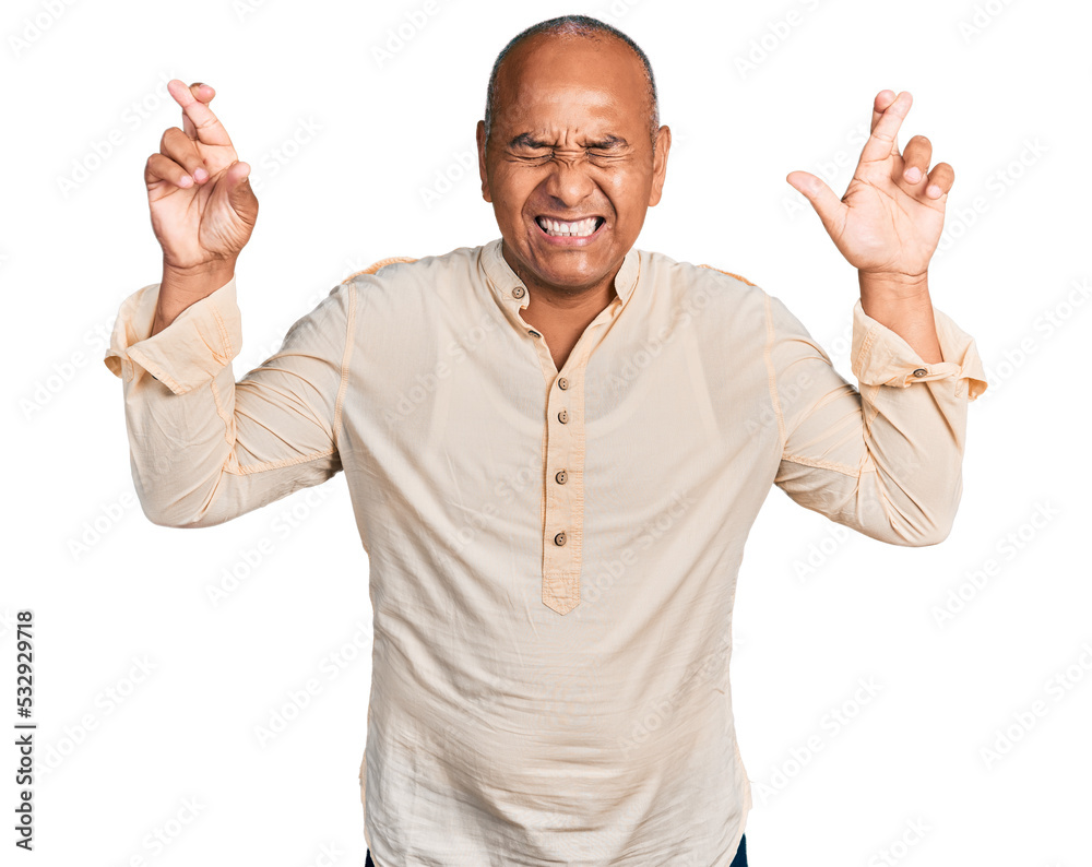 Hispanic middle age man wearing boho shirt gesturing finger crossed smiling with hope and eyes closed. luck and superstitious concept.