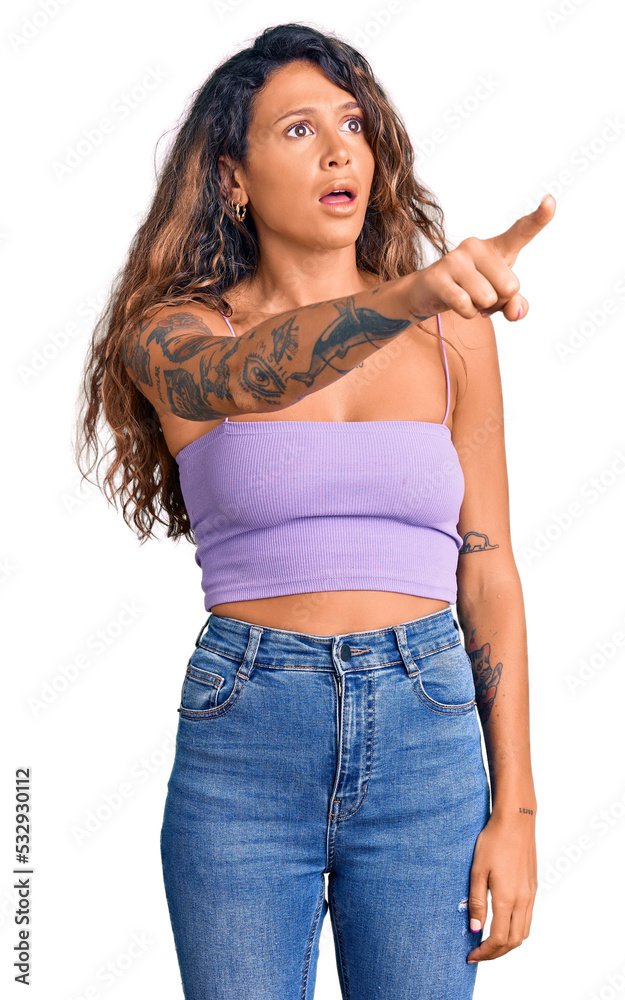 Young hispanic woman with tattoo wearing casual clothes pointing with finger surprised ahead, open mouth amazed expression, something on the front Young hispanic woman with tattoo wearing casual clothes pointing with finger surprised ahead, open mouth amazed expression, something on the front