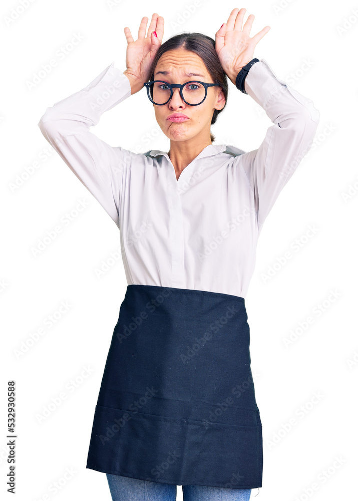 Beautiful brunette young woman wearing professional waitress apron doing bunny ears gesture with hands palms looking cynical and skeptical. easter rabbit concept. Beautiful brunette young woman wearing professional waitress apron doing bunny ears gesture with hands palms looking cynical and skeptical. easter rabbit concept.