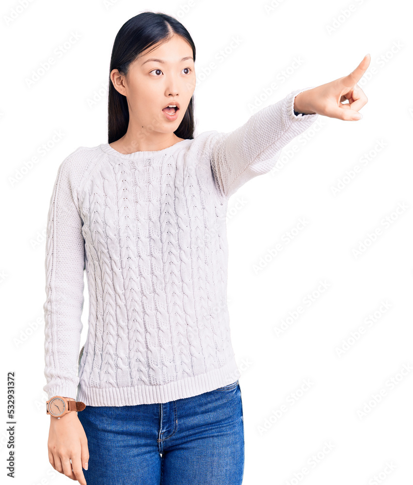 Young beautiful chinese woman wearing casual sweater pointing with finger surprised ahead, open mouth amazed expression, something on the front