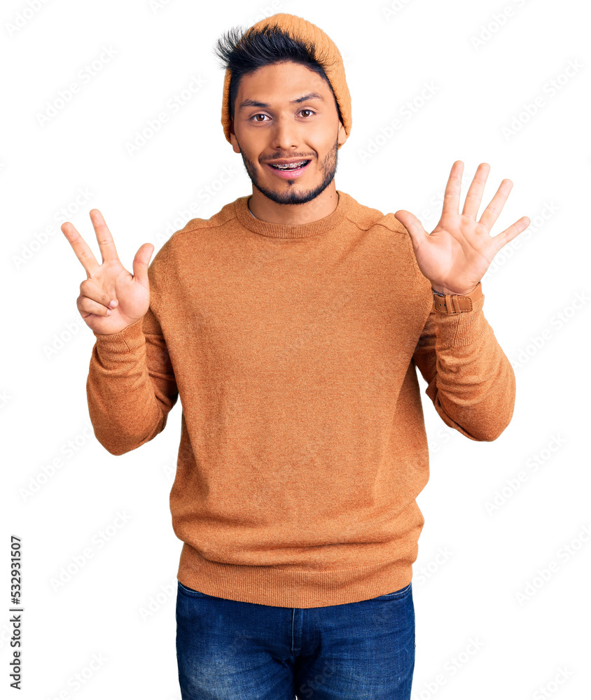 Handsome latin american young man wearing winter sweater and wool hat showing and pointing up with fingers number eight while smiling confident and happy. Handsome latin american young man wearing winter sweater and wool hat showing and pointing up with fingers number eight while smiling confident and happy.