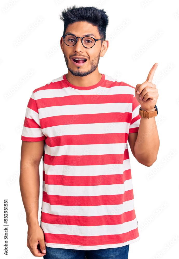 Handsome latin american young man wearing casual clothes and glasses pointing finger up with successful idea. exited and happy. number one. Handsome latin american young man wearing casual clothes and glasses pointing finger up with successful idea. exited and happy. number one.