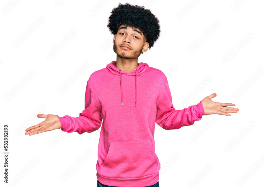 Young african american man with afro hair wearing casual pink sweatshirt smiling showing both hands open palms, presenting and advertising comparison and balance Young african american man with afro hair wearing casual pink sweatshirt smiling showing both hands open palms, presenting and advertising comparison and balance