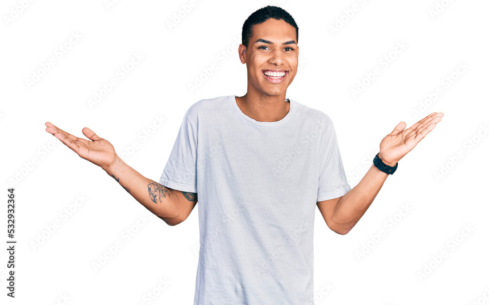 Young hispanic man wearing casual white t shirt smiling showing both hands open palms, presenting and advertising comparison and balance Young hispanic man wearing casual white t shirt smiling showing both hands open palms, presenting and advertising comparison and balance