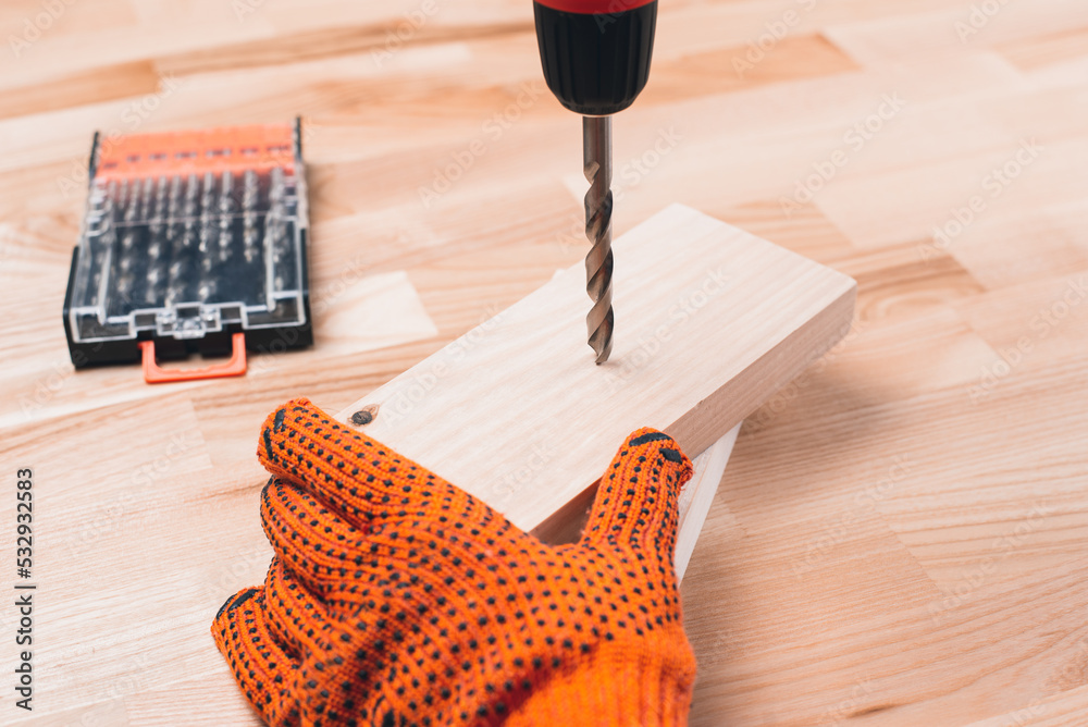 Screwdriver drill in hand. Gloved hands. The master drills wooden blocks. A carpenter Screwdriver drill in hand. Gloved hands. The master drills wooden blocks. A carpenter