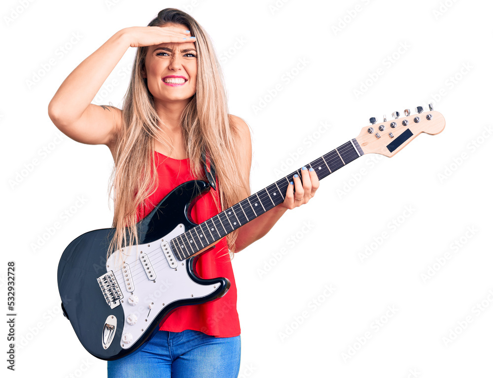 Young beautiful blonde woman playing electric guitar stressed and frustrated with hand on head, surprised and angry face