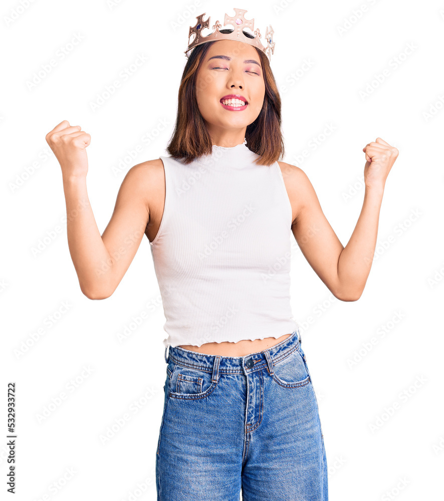 Young beautiful chinese girl wearing princess crown very happy and excited doing winner gesture with arms raised, smiling and screaming for success. celebration concept. Young beautiful chinese girl wearing princess crown very happy and excited doing winner gesture with arms raised, smiling and screaming for success. celebration concept.