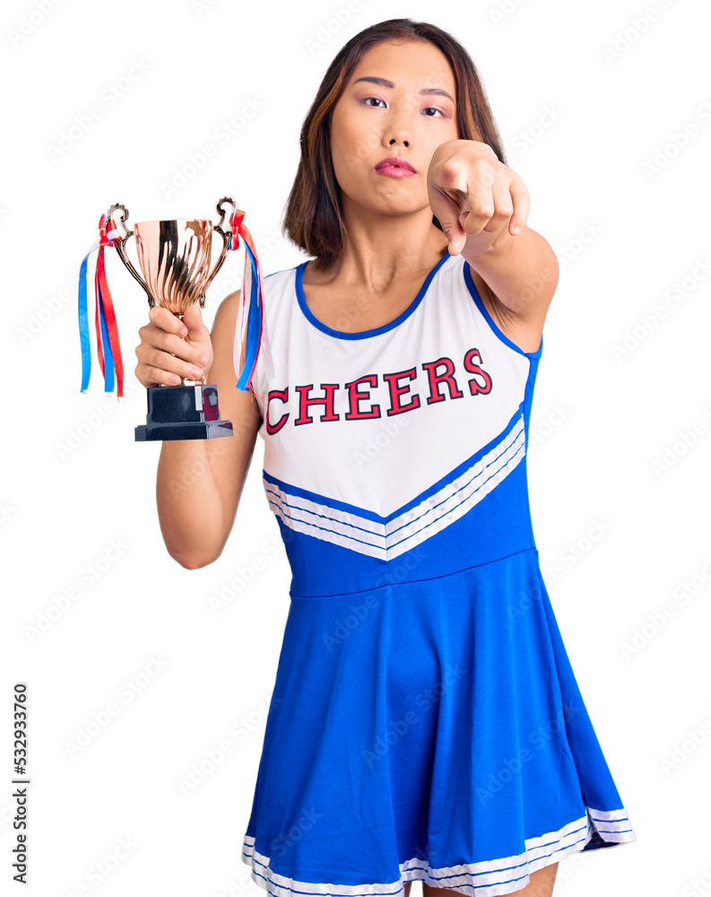 Youn beautiful asian girl wearing cheerleader uniform holding champion trophy pointing with finger to the camera and to you, confident gesture looking serious Youn beautiful asian girl wearing cheerleader uniform holding champion trophy pointing with finger to the camera and to you, confident gesture looking serious