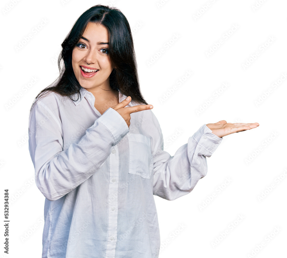 Beautiful hispanic woman wearing casual white shirt amazed and smiling to the camera while presenting with hand and pointing with finger. Beautiful hispanic woman wearing casual white shirt amazed and smiling to the camera while presenting with hand and pointing with finger.