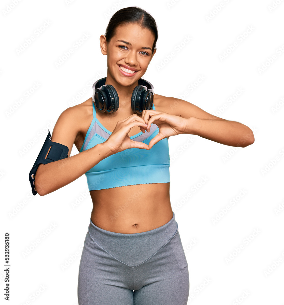 Beautiful hispanic woman wearing sportswear and headphones smiling in love showing heart symbol and shape with hands. romantic concept. Beautiful hispanic woman wearing sportswear and headphones smiling in love showing heart symbol and shape with hands. romantic concept.