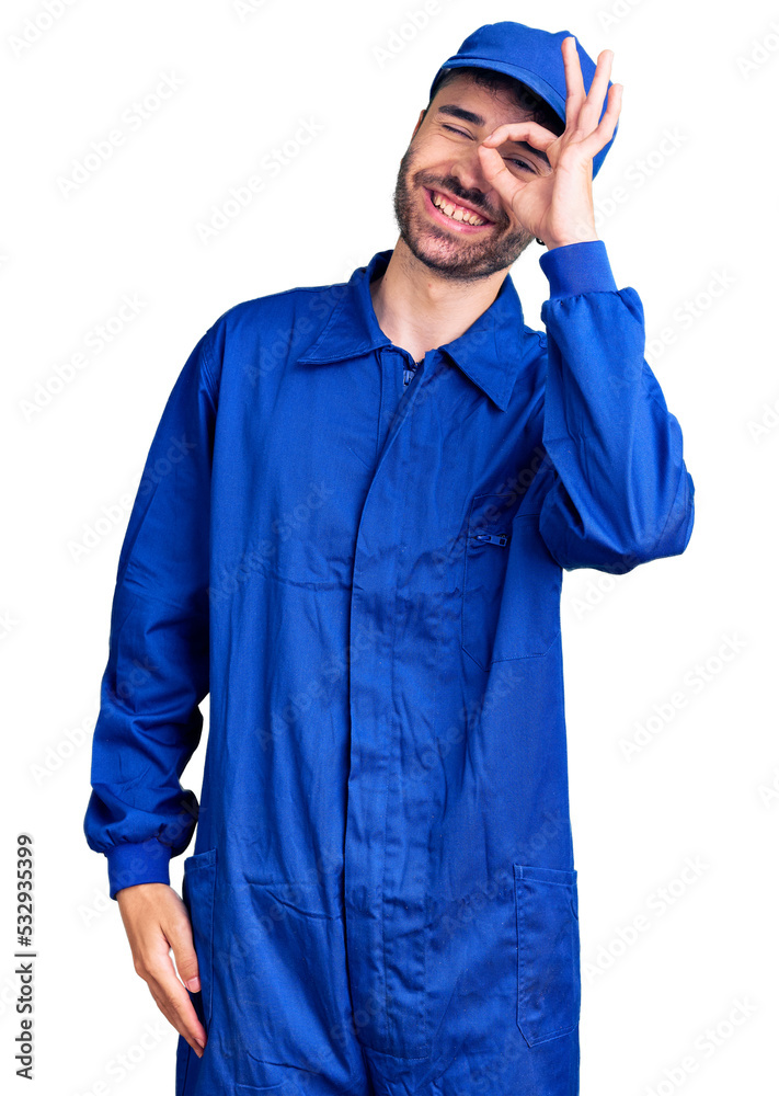 Young hispanic man wearing painter uniform smiling happy doing ok sign with hand on eye looking through fingers Young hispanic man wearing painter uniform smiling happy doing ok sign with hand on eye looking through fingers