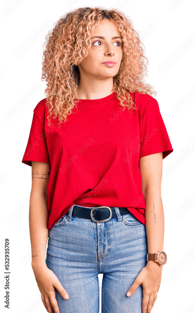 Young blonde woman with curly hair wearing casual red tshirt smiling looking to the side and staring away thinking. Young blonde woman with curly hair wearing casual red tshirt smiling looking to the side and staring away thinking.