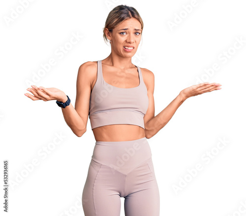 Beautiful caucasian woman wearing sportswear clueless and confused with open arms, no idea concept.