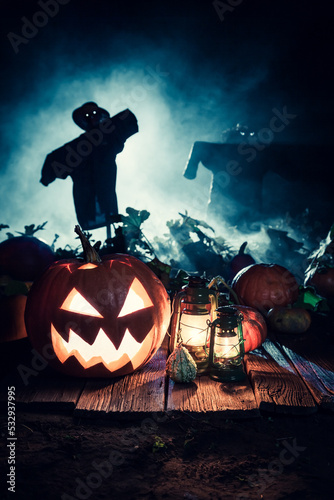 Halloween pumpkin with blue mist and scarecrows at night.
