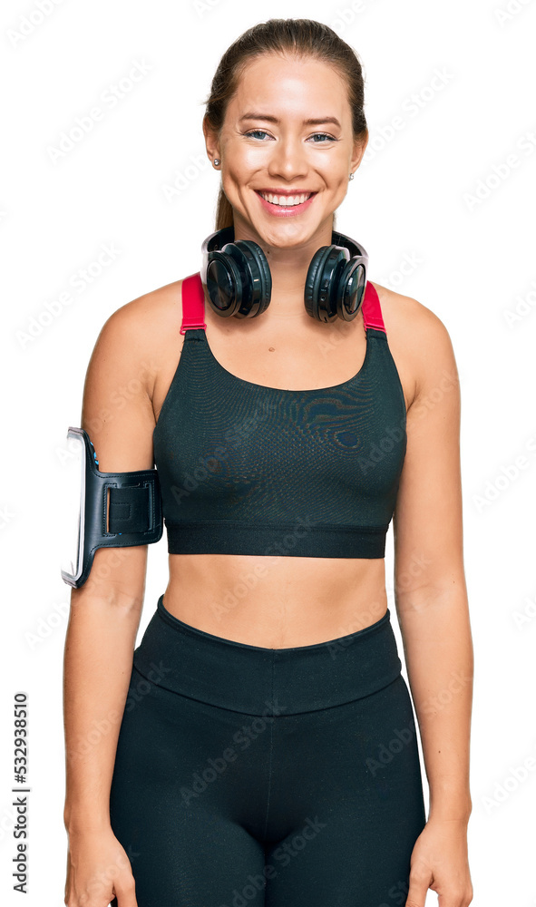 Beautiful blonde woman wearing gym clothes and using headphones with a happy and cool smile on face. lucky person. Beautiful blonde woman wearing gym clothes and using headphones with a happy and cool smile on face. lucky person.