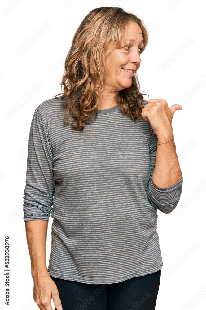 Middle age blonde woman wearing casual clothes smiling with happy face looking and pointing to the side with thumb up.