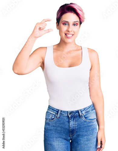 Young beautiful woman with pink hair wearing casual clothes smiling and confident gesturing with hand doing small size sign with fingers looking and the camera. measure concept.