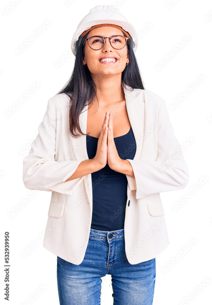 Young beautiful latin girl wearing architect hardhat and glasses begging and praying with hands together with hope expression on face very emotional and worried. begging.