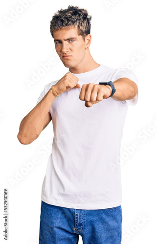 Young handsome man wearing casual white tshirt punching fist to fight, aggressive and angry attack, threat and violence