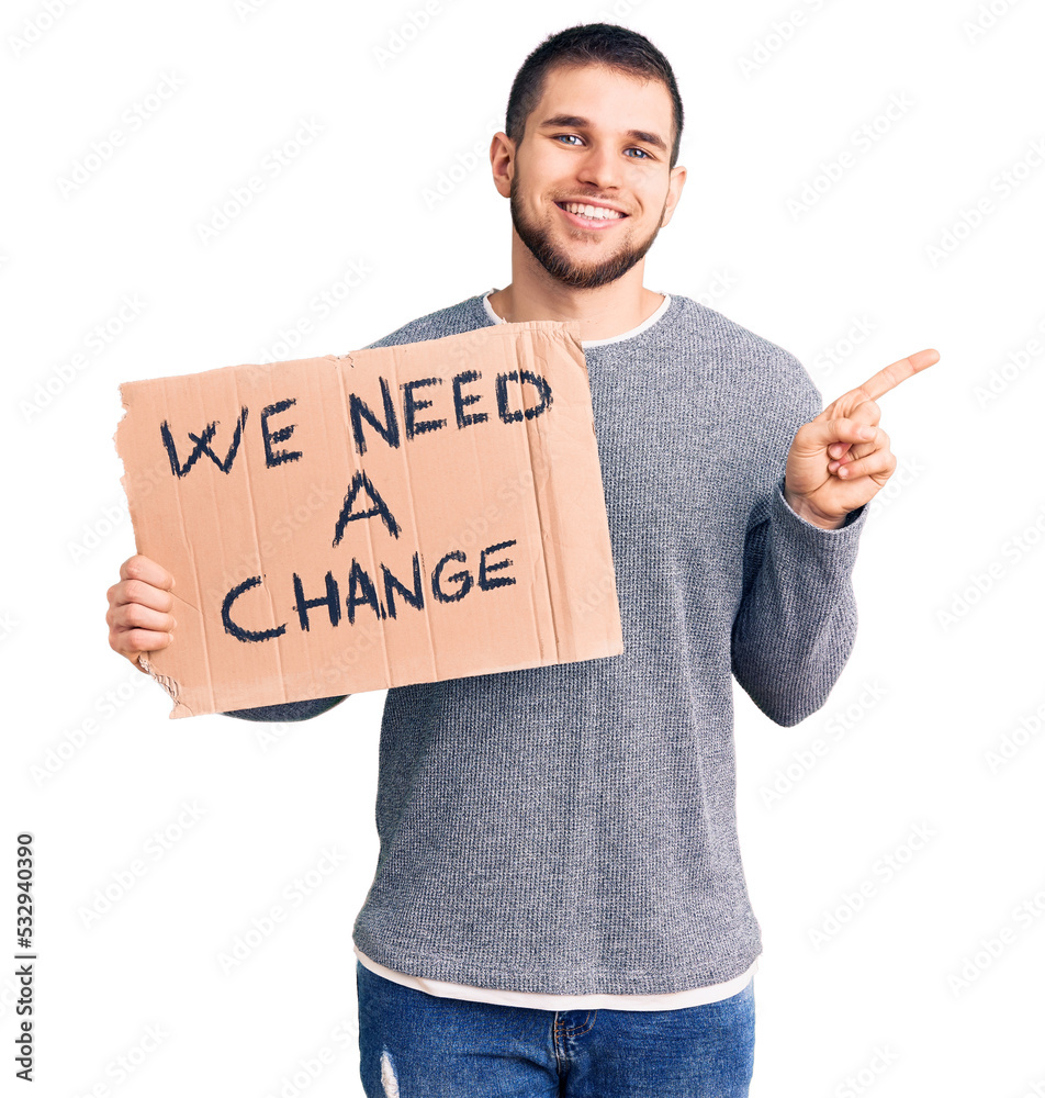 Young handsome man holding we need a change banner smiling happy pointing with hand and finger to the side