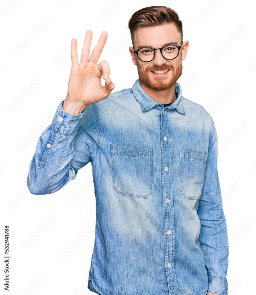 Young redhead man wearing casual denim shirt smiling positive doing ok sign with hand and fingers. successful expression. Young redhead man wearing casual denim shirt smiling positive doing ok sign with hand and fingers. successful expression.