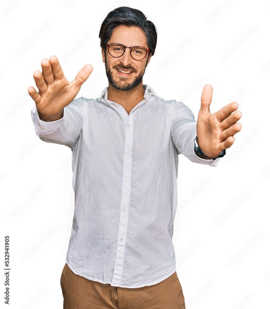 Young hispanic man wearing business shirt and glasses looking at the camera smiling with open arms for hug. cheerful expression embracing happiness. Young hispanic man wearing business shirt and glasses looking at the camera smiling with open arms for hug. cheerful expression embracing happiness.