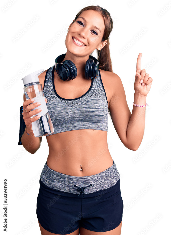 Young beautiful hispanic woman wearing sportswear holding water bottle surprised with an idea or question pointing finger with happy face, number one