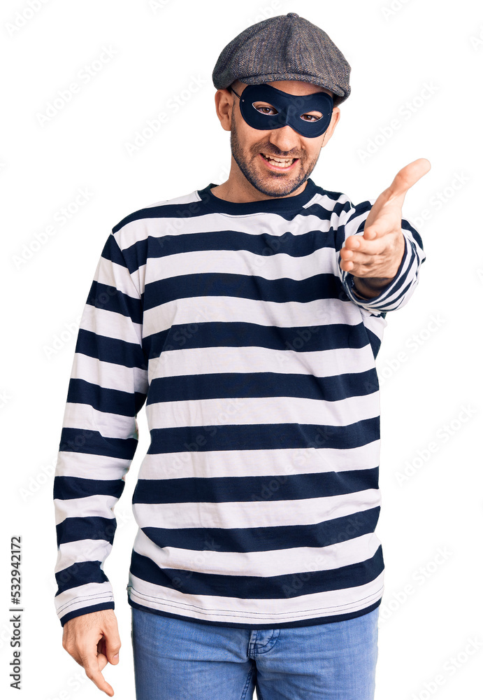 Young handsome man wearing burglar mask smiling friendly offering handshake as greeting and welcoming. successful business. Young handsome man wearing burglar mask smiling friendly offering handshake as greeting and welcoming. successful business.
