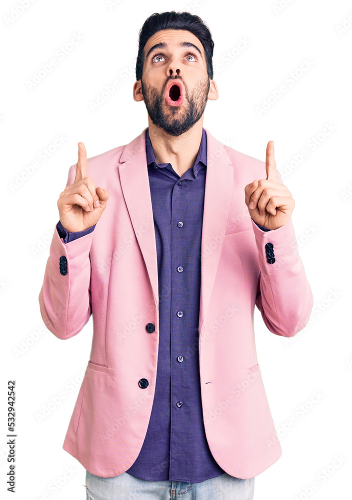 Young handsome man with beard wearing elegant jacket amazed and surprised looking up and pointing with fingers and raised arms. Young handsome man with beard wearing elegant jacket amazed and surprised looking up and pointing with fingers and raised arms.