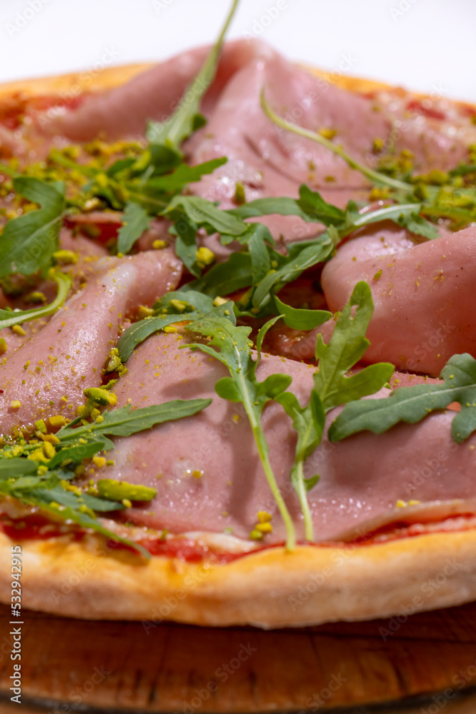 Pizza with ham, arugula and pistachios served on wooden platter Pizza with ham, arugula and pistachios served on wooden platter