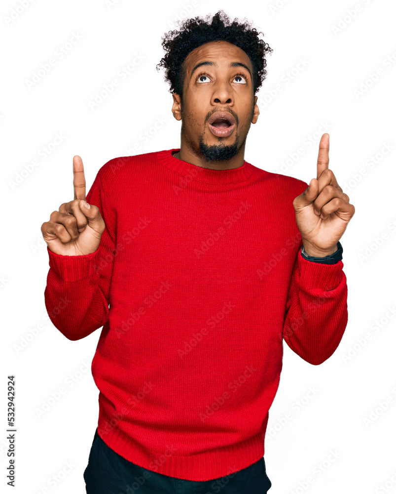 Young african american man with beard wearing casual winter sweater amazed and surprised looking up and pointing with fingers and raised arms. Young african american man with beard wearing casual winter sweater amazed and surprised looking up and pointing with fingers and raised arms.