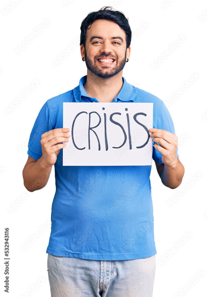 Young hispanic man holding crisis message paper looking positive and happy standing and smiling with a confident smile showing teeth