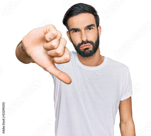 Young hispanic man wearing casual white t shirt looking unhappy and angry showing rejection and negative with thumbs down gesture. bad expression.