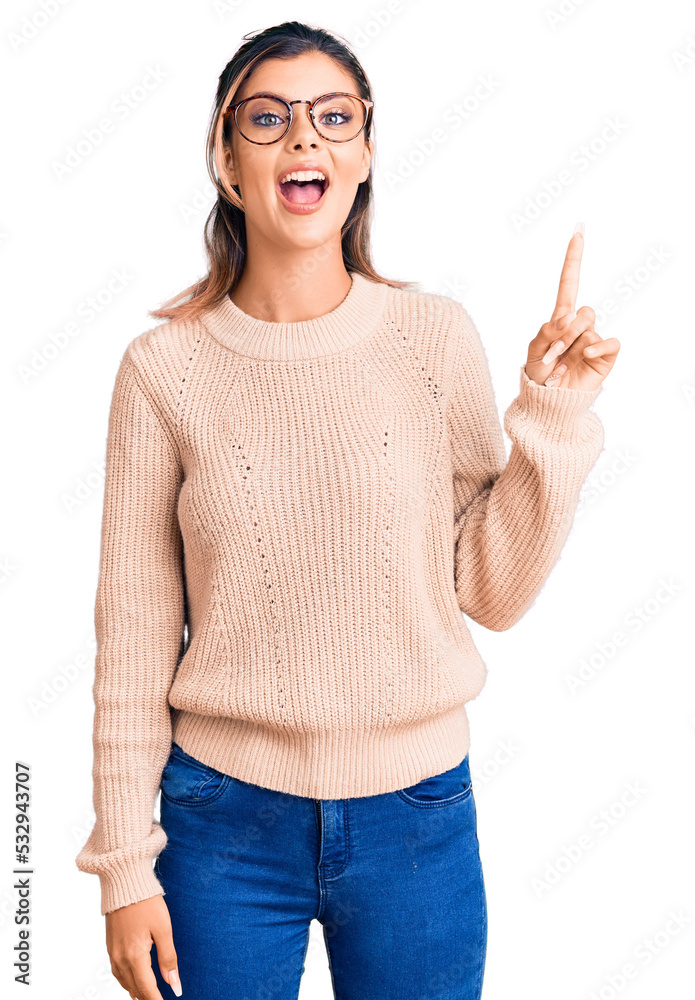 Young beautiful woman wearing casual winter sweater and glasses pointing finger up with successful idea. exited and happy. number one. Young beautiful woman wearing casual winter sweater and glasses pointing finger up with successful idea. exited and happy. number one.