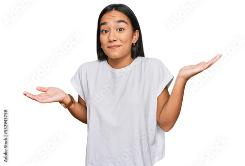 Young asian woman wearing casual white t shirt clueless and confused expression with arms and hands raised. doubt concept. photo